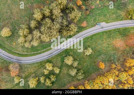 Leere kurvenreiche Asphaltfahrradbahn führt durch die malerische Herbstlandschaft. Drohnenfoto. Stockfoto