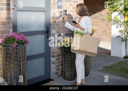 Frau kommt mit Lebensmitteln nach Hause und gibt einen Code ein, um die Tür zu betreten Stockfoto