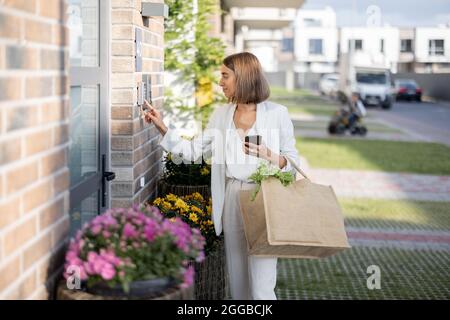 Frau kommt mit Lebensmitteln nach Hause und gibt einen Code ein, um die Tür zu betreten Stockfoto