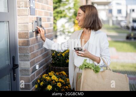 Frau kommt mit Lebensmitteln nach Hause und gibt einen Code ein, um die Tür zu betreten Stockfoto