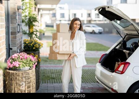 Junge Geschäftsfrau, die Pakete von einem Kofferraum abholt und mit dem Auto nach Hause kommt. Konzept, Waren online zu kaufen und nach Hause zu liefern Stockfoto