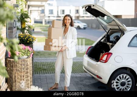 Frau mit Paketen in der Nähe ihres Autos und ihres Hauses Stockfoto