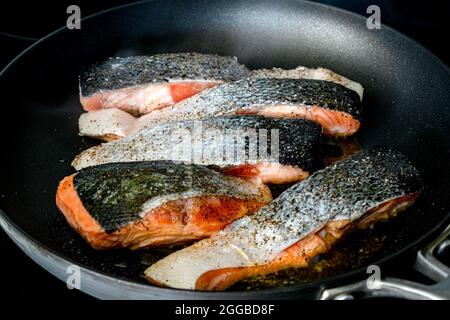 Rohe Lachsfilets in einer beschichteten Pfanne braten: Ungekochte Fischfilets, gewürzt mit Salz und Pfeffer in einer Pfanne Stockfoto