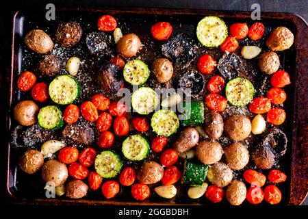 Italienischer Ofen Gebratenes Gemüse auf einem Blatt Pfanne: Geröstete Traubentomaten, Zucchini, Pilze, rote Kartoffeln, Knoblauchzehen Stockfoto