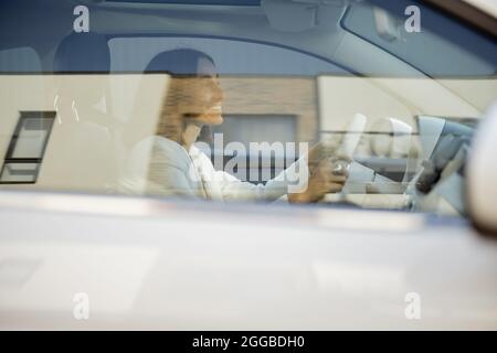 Porträt einer jungen Geschäftsfrau in weißem Anzug mit Auto, Blick durch die Seitenscheibe Stockfoto
