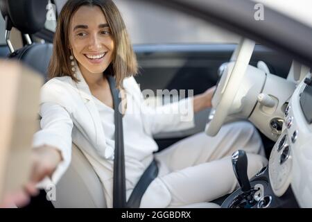 Frau, die unterwegs ein Paket durch das Fahrzeugfenster erhält Stockfoto