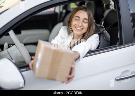 Frau, die unterwegs ein Paket durch das Fahrzeugfenster erhält Stockfoto