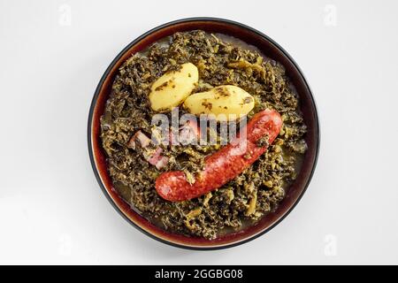 Traditionelle deutsche würzige Wurst mit frisch gekochtem oder geschmortem Grünkohl und zwei Babykartoffeln in der Ansicht von oben auf einem Steingutteller, der auf Weiß isoliert ist Stockfoto