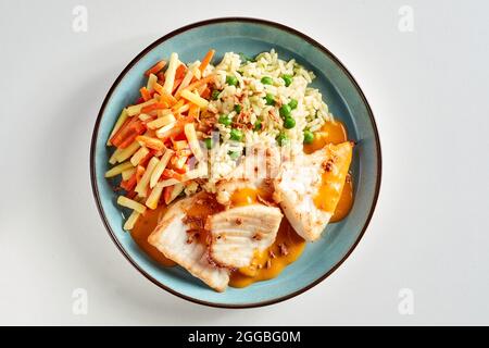 Im Ofen gebackene Cichlid-Fischfilets, serviert mit gemischtem Gemüse und beträufelt mit einer herzhaften Sauce in einer Ansicht von oben nach unten auf einem Teller über Weiß für Menü adv Stockfoto