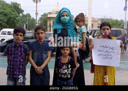 Frau aus Shahdara hält Plakate, die Kinder zum Verkauf beschreiben, während sie ihre Kinder während einer Protestdemonstration vor dem Gebäude der Punjab-Versammlung in Lahore am Montag, dem 30. August 2021, verkaufen möchte. Stockfoto