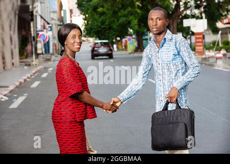 Junger Geschäftsmann steht im Freien in traditioneller Kleidung und schüttelt sich die Hände, während sein Partner lächelt. Stockfoto