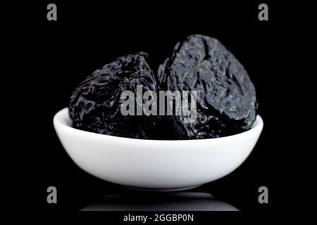 Mehrere süße dunkle Pflaumen in einer Keramikschale, Nahaufnahme, isoliert auf Schwarz. Stockfoto