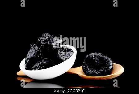 Mehrere süße dunkle Pflaumen in einer Keramikschale, Nahaufnahme, isoliert auf Schwarz. Stockfoto