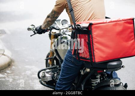 Zugeschnittenes Bild eines Kuriers mit roter isolierter Tasche, der auf dem Motorrad fährt, Blick von hinten Stockfoto