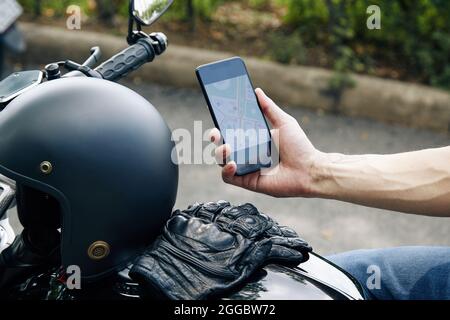 Nahaufnahme des Motorradfahrers, der die Kartenanwendung auf dem Smartphone überprüft, wenn er die Adresse des Kunden sucht Stockfoto