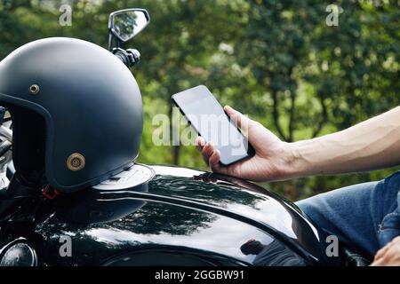 Nahaufnahme des Motorradfahrers, der auf dem Fahrzeug sitzt und die Anwendung auf dem Smartphone überprüft Stockfoto