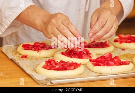 Die Frau auf dem Bild macht gefüllte Obstkuchen. Hände füllen Kuchen Hefeteig mit Erdbeeren. Arbeiten Sie in der Bäckerei. Stockfoto