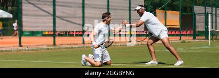 Aufgeregte multiethnische Tennisspieler, die auf dem Platz die Hände schütteln, Banner Stockfoto