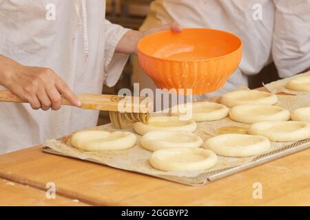 Die Frau auf dem Bild macht gefüllte Kuchen. Hände, die Schutzhandschuhe tragen, beschichten den Pie-Teig mit rohem Ei. Arbeiten Sie in der Bäckerei. Stockfoto