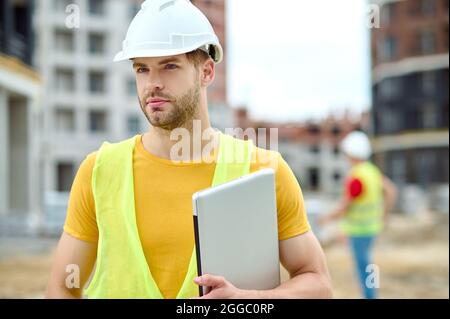 Gut aussehender, fokussierter Bauarbeiter mit Kopfbedeckung und Blick in die Zukunft Stockfoto
