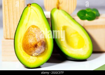 Hälften von reifen Avocado und Micro Green auf Holzbrett serviert auf dem Tisch, weißer Hintergrund, gesunde ölige Lebensmittel, Keto-Diät, Nahaufnahme. Stockfoto