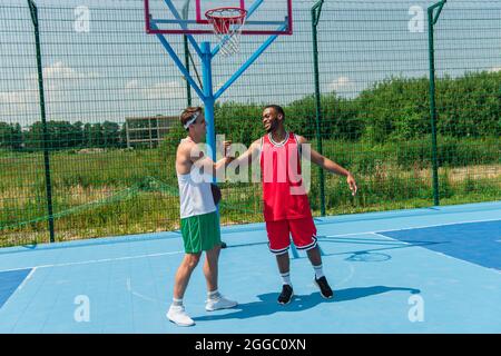 Lächelnde multiethnische Sportler, die sich auf dem Streetball-Spielplatz die Hände schütteln Stockfoto