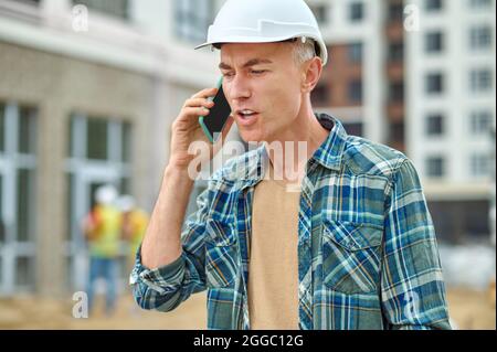 Grauhaariger männlicher Baumeister, der draußen auf seinem Handy spricht Stockfoto