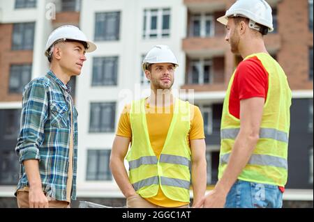 Drei Bauherren in Schutzhelmen bei einem Gespräch im Freien Stockfoto