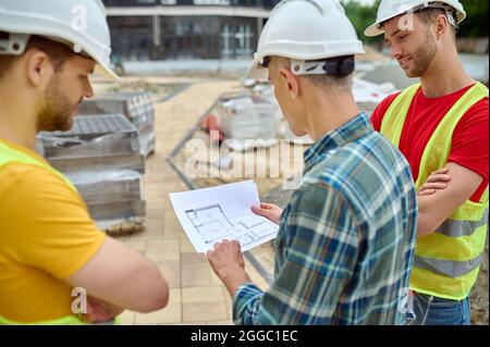 Drei kaukasische Männer in Schutzhelmen, die Baupläne studieren Stockfoto