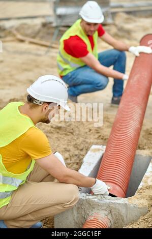 Zwei erfahrene Arbeiter, die eine Abwasserkanalleitung für Wohngebäude installierten Stockfoto