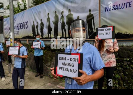 Metro Manila, Philippinen. August 2021. Mitarbeiter des Gesundheitswesens tragen während eines Protestes zum National Heroes Day vor dem St. Luke's Medical Center in Quezon City Schilder. Die Gruppe forderte die Regierung auf, Mittel für Leistungen und einen angemessenen Schutz für medizinisches Personal freizugeben, das angesichts der Zunahme der COVID-19-Fälle im Land weiterhin gefährdet ist. Kredit: Majority World CIC/Alamy Live Nachrichten Stockfoto