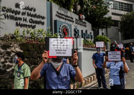 Metro Manila, Philippinen. August 2021. Mitarbeiter des Gesundheitswesens tragen während eines Protestes zum National Heroes Day vor dem St. Luke's Medical Center in Quezon City Schilder. Die Gruppe forderte die Regierung auf, Mittel für Leistungen und einen angemessenen Schutz für medizinisches Personal freizugeben, das angesichts der Zunahme der COVID-19-Fälle im Land weiterhin gefährdet ist. Kredit: Majority World CIC/Alamy Live Nachrichten Stockfoto