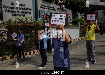 Metro Manila, Philippinen. August 2021. Mitarbeiter des Gesundheitswesens tragen während eines Protestes zum National Heroes Day vor dem St. Luke's Medical Center in Quezon City Schilder. Die Gruppe forderte die Regierung auf, Mittel für Leistungen und einen angemessenen Schutz für medizinisches Personal freizugeben, das angesichts der Zunahme der COVID-19-Fälle im Land weiterhin gefährdet ist. Kredit: Majority World CIC/Alamy Live Nachrichten Stockfoto