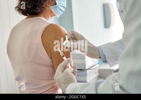 Ältere Dame mit Gesichtsmask, die in der Klinik eine Impfung mit Covid19 erhalten hat. Stockfoto