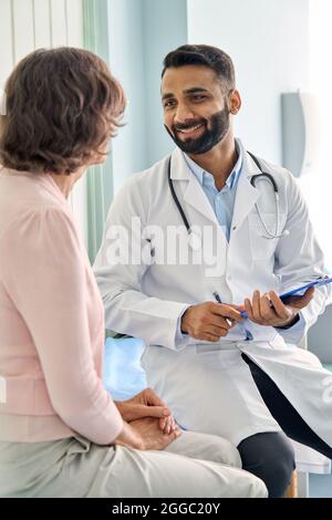Glücklicher indischer Arzt, der weibliche ältere Patientin im Krankenhaus konsultiert. Vertikal. Stockfoto