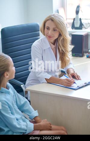 Fokussierter Arzt, der während der Kinderkonsultation am Schreibtisch sitzt Stockfoto