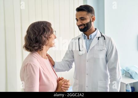 Fröhlicher indischer lateinischer Arzt, der weibliche ältere Patientin im Krankenhaus konsultiert. Stockfoto