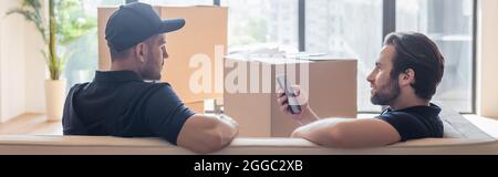mover mit Smartphone im Gespräch mit Kollegen, während auf dem Sofa in der Nähe von Kartons sitzen, Banner Stockfoto
