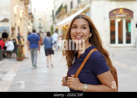 Wunderschöne, entzückt lächelnde Touristenfrau, die auf einem Tagesausflug im Sommer durch die Stadt schlendert Stockfoto