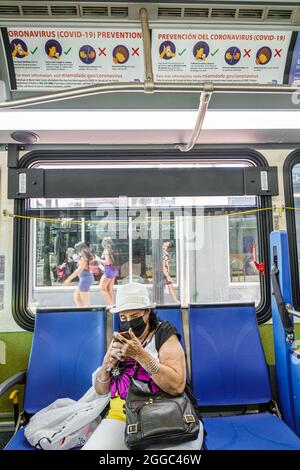 Miami Beach Florida Miami-Dade Metrobus öffentlichen Verkehrsmitteln an Bord innen Senioren Passagier Fahrer tragen Maske Texting suchen Stockfoto