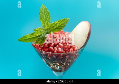 Gesunde Granatapfelkerne im Cocktailglas mit Apfel und Minze auf blauem Hintergrund Stockfoto