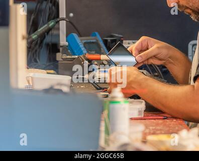 Seitenansicht eines nicht erkennbaren hispanischen Mannes, der einen Kamerabildschirm im Service-Shop zerlegt. Stockfoto