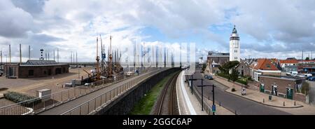 Leuchtturm, Eisenbahnstrecke mit Fußgängerpromenade und historische Segelschiffe im niederländischen Hafen Harlingen mit schönem blau bewölktem Himmel Stockfoto