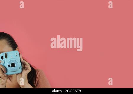 Weibliche junge Erwachsene mit einer Retro-Kamera. Instant Polaroid Blue Kamera: FUJIFILM INSTAX Mini 11 Instant Film Kamera - Kopierraum Stockfoto