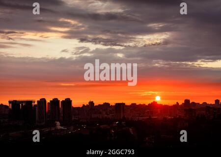 Die schillernde Scheibe der Morgensonne überflutet am frühen Sommermorgen die Stadtsilhouetten von Häusern in leuchtender rot-oranger Farbe. Stockfoto