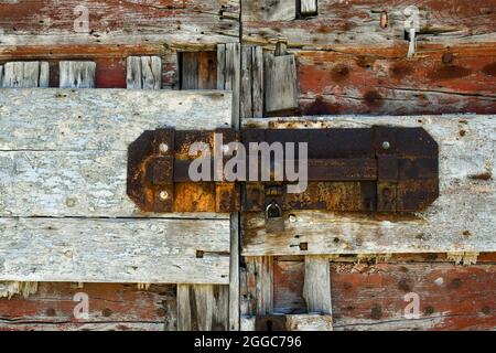 Detail einer alten, verwitterten Holztür, geschlossen mit einem rostigen Schloss, Italien Stockfoto