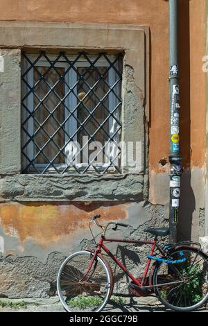 Ein altes rostiges Fahrrad gegen die Wand eines alten Gebäudes mit einem Fenster, das von einem Eisengitter geschlossen wurde, Livorno, Toskana, Italien Stockfoto