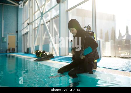 Männlicher Taucher im Tauchanzug, der am Pool sitzt Stockfoto