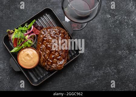 Gegrilltes Schweinesteak mit Sauce, Glas Wein und Gemüse in einer Pfanne mit Platz für Text Stockfoto