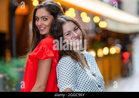 Zwei niedliche und wunderschöne Frauen stehen zusammen auf verschwommenem Hintergrund mit Bokeh-Licht Stockfoto